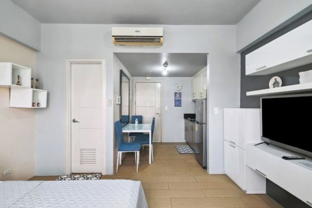 Une chambre d’hôtel de taille réduite, comprenant un lit, un bureau, une chaise, un coin cuisine et un téléviseur.