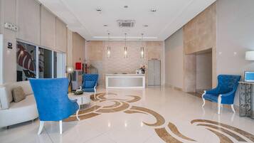 Una hall moderna con una reception, poltrone blu, un divano bianco e un motivo decorativo sul pavimento.
