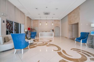 Un hall d’entrée moderne avec un comptoir d’accueil, des fauteuils bleus, un canapé blanc et un motif décoratif sur le sol.