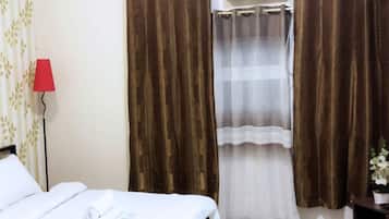 Une chambre d’hôtel avec un lit, une lampe rouge, des rideaux marron, un climatiseur et une petite table sur laquelle est posée une plante.