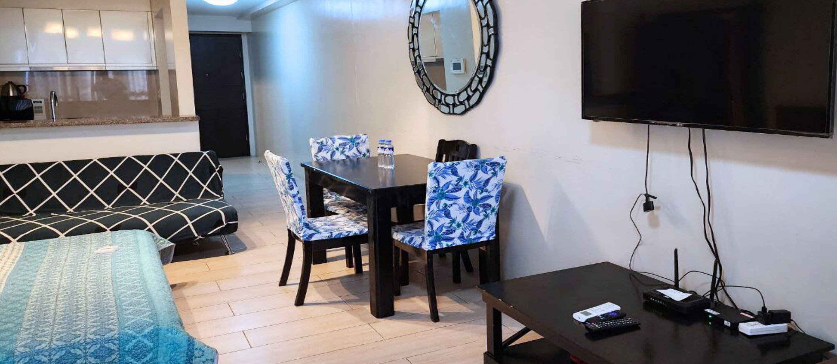 A hotel room with a bed, a dining table with chairs, a TV, and a desk with a computer and phone.