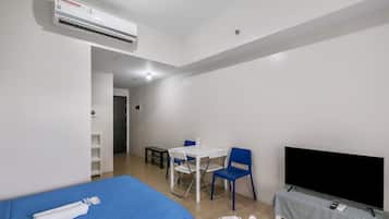 A hotel room with a bed, a desk with chairs, a television, and an air conditioning unit.