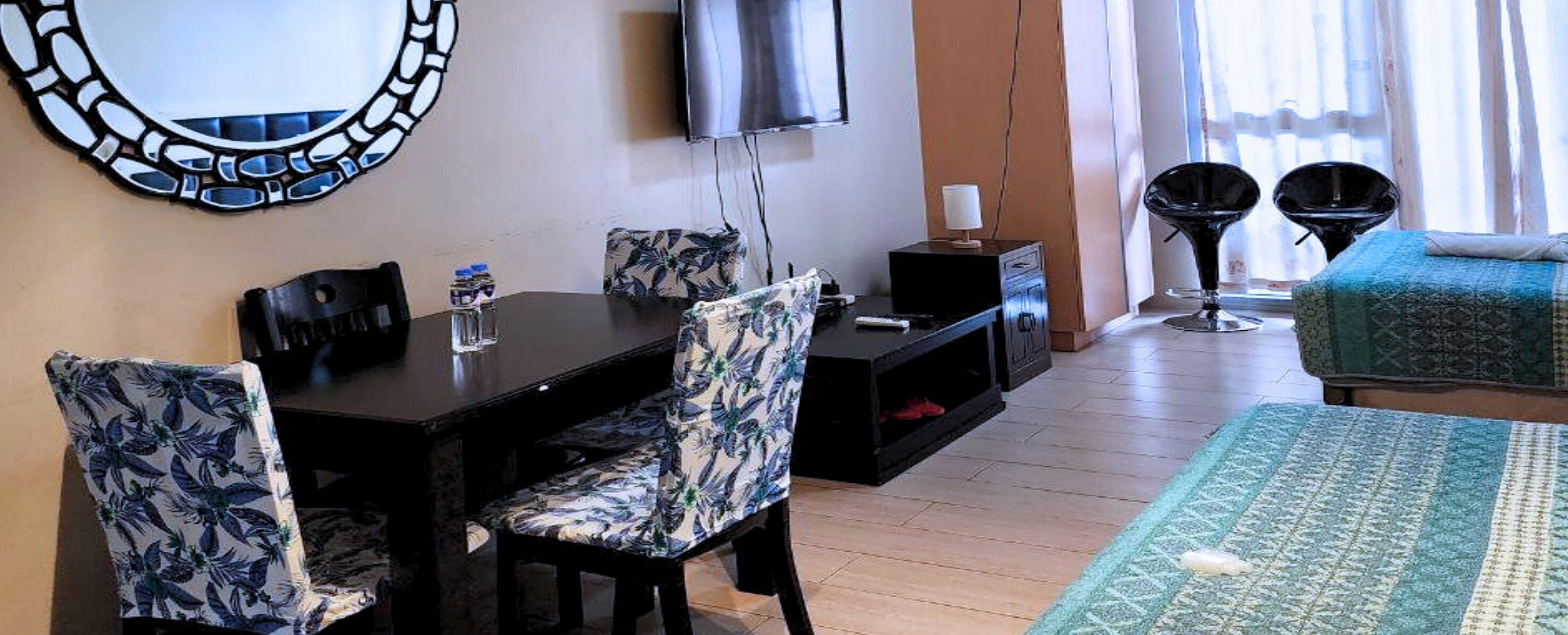 Habitación de hotel con una mesa de comedor, sillas, televisor, cama y ventana con cortinas.