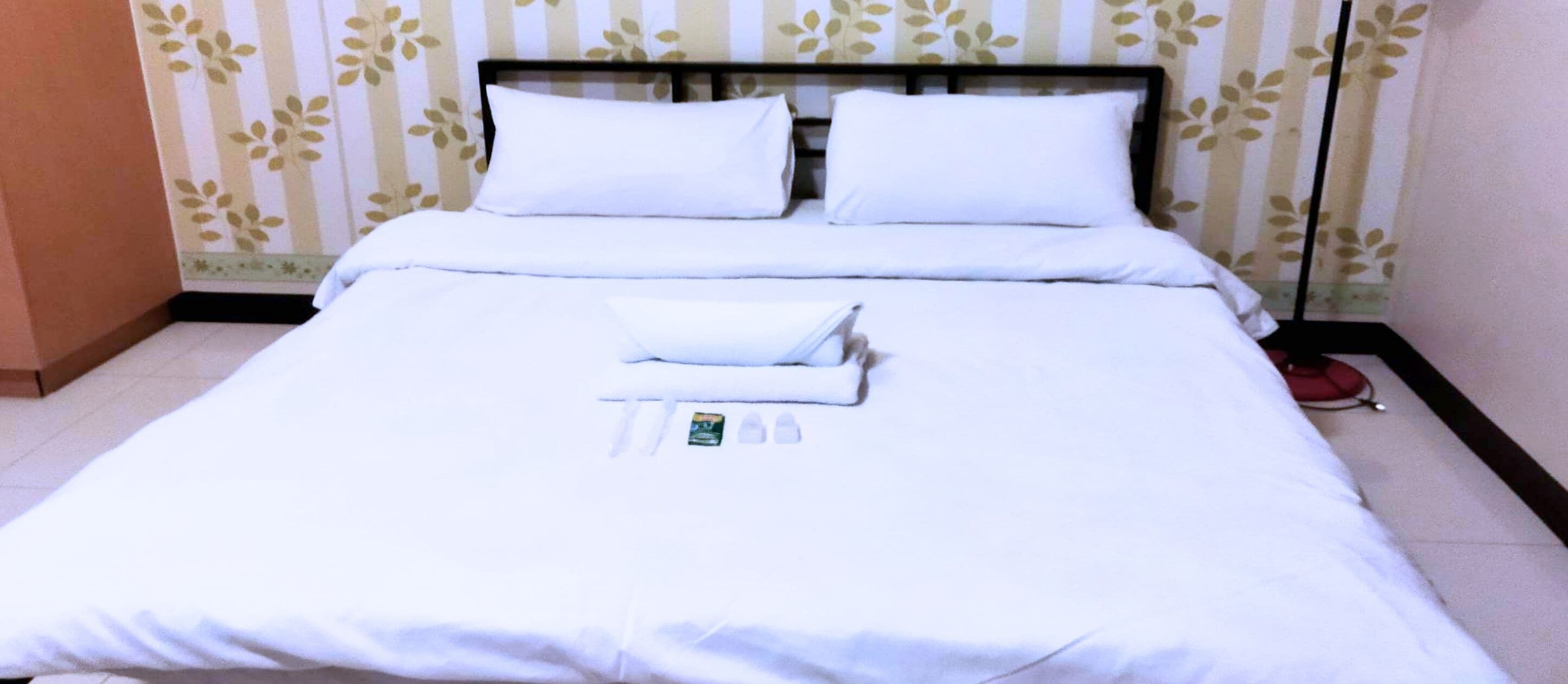 A neatly made bed with white linens, pillows, and a folded towel.