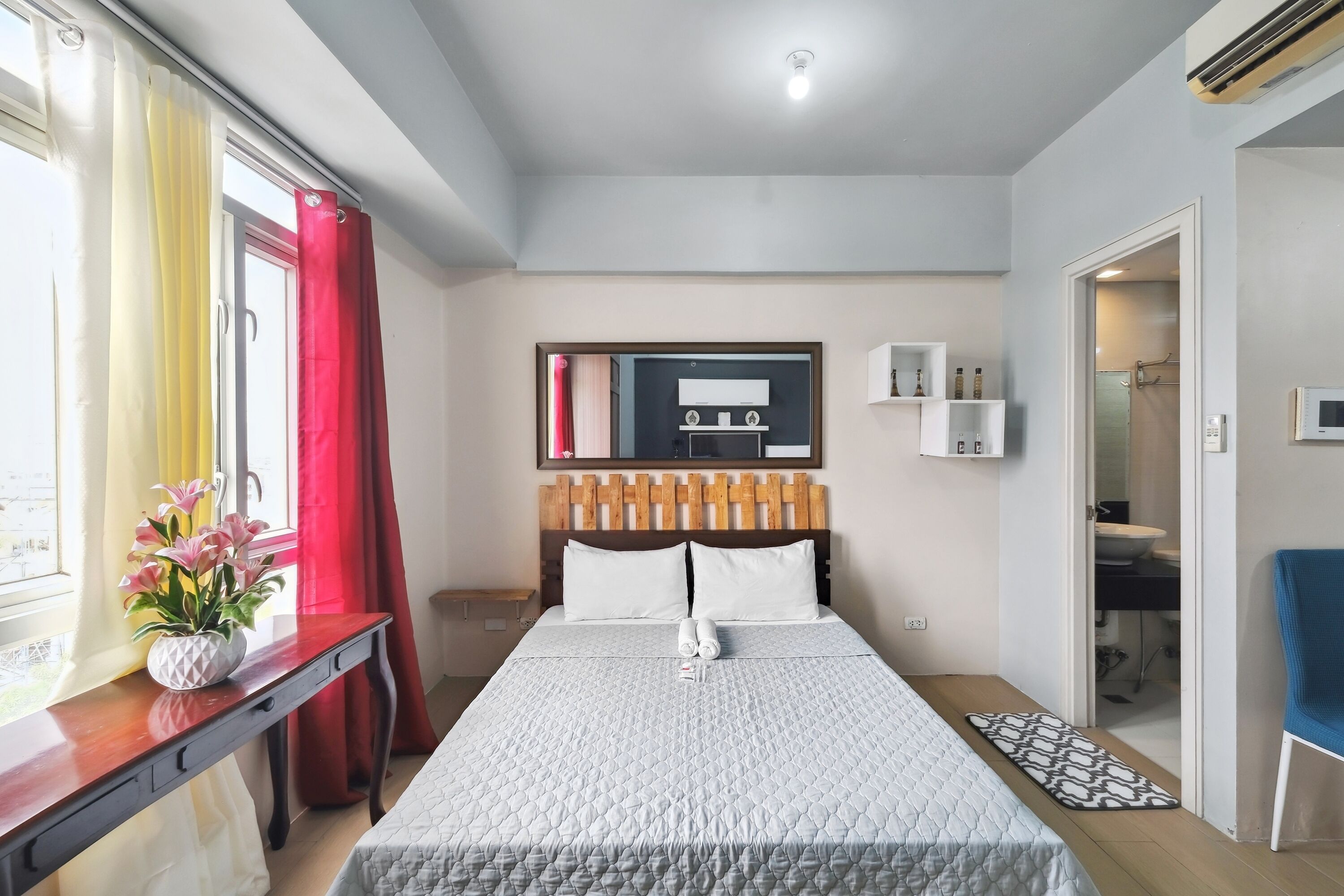 A hotel room with a bed, bedside table, and a window with curtains.