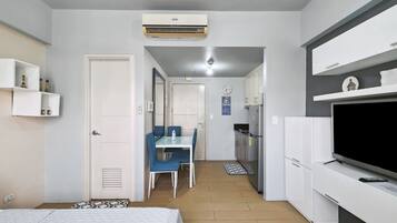A compact hotel room with a bed, a kitchenette, a dining area, and a TV.