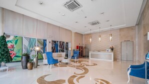 Un hall d’hôtel moderne avec un comptoir d’accueil, des chaises bleues, un canapé blanc et un motif décoratif sur le sol.