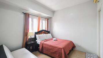 A bedroom with a bed, a nightstand, a lamp, a window with curtains, and a small rug.