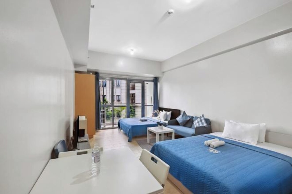 Une chambre d’hôtel avec un lit, un bureau et une chaise. Il y a une fenêtre qui donne sur les bâtiments à l’extérieur.