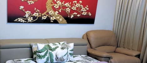 Un dormitorio con cama, sofá, sillón y un cuadro colgado en la pared de un árbol con flores.