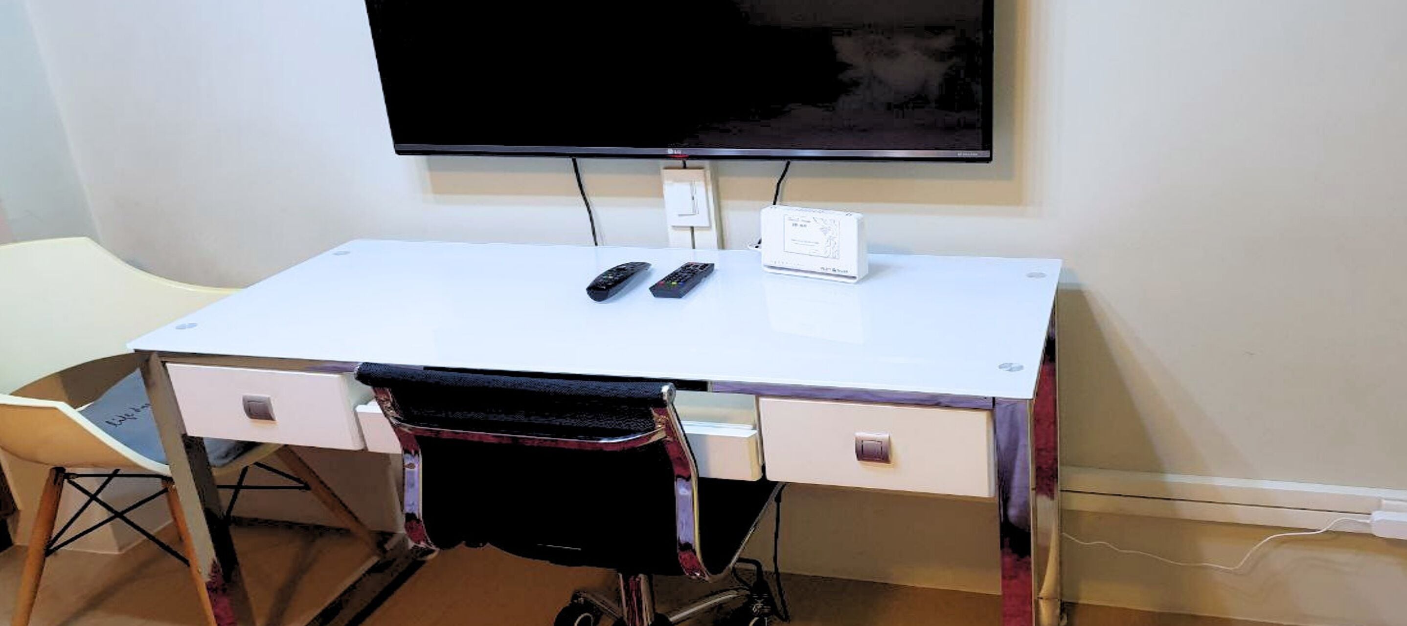 Un escritorio blanco con dos controles remotos, una regleta y una silla de ruedas al frente.