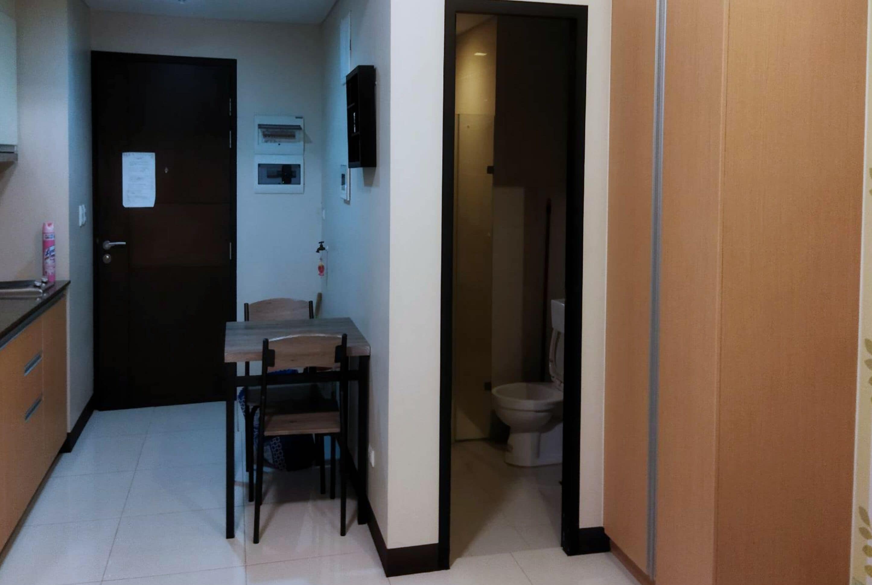 Un corridoio stretto con una piccola zona pranzo, che include un tavolo e sedie, una porta scura e un bagno visibile attraverso una porta aperta.