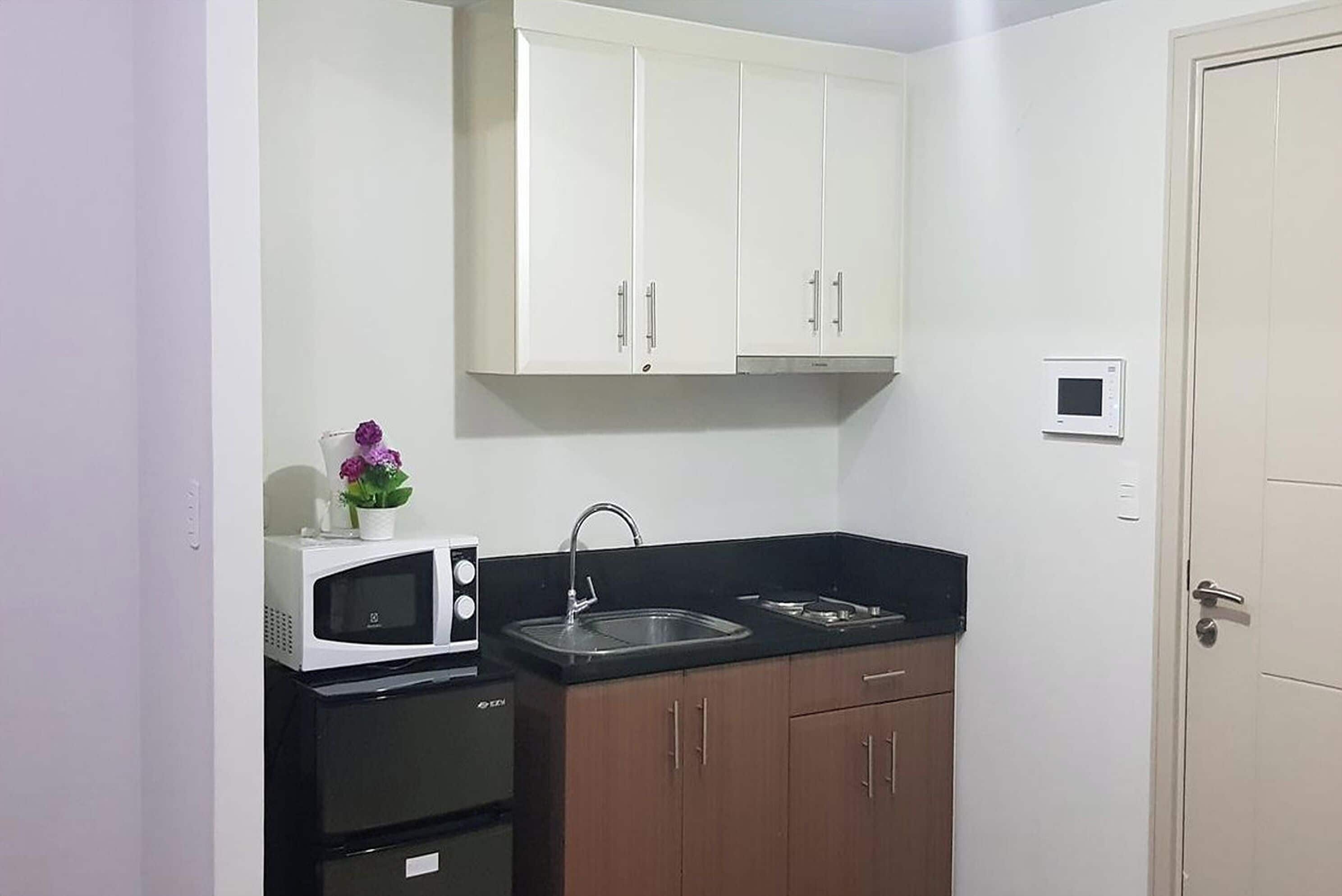 A compact kitchen with white cabinets, a microwave, a sink, and a small refrigerator.