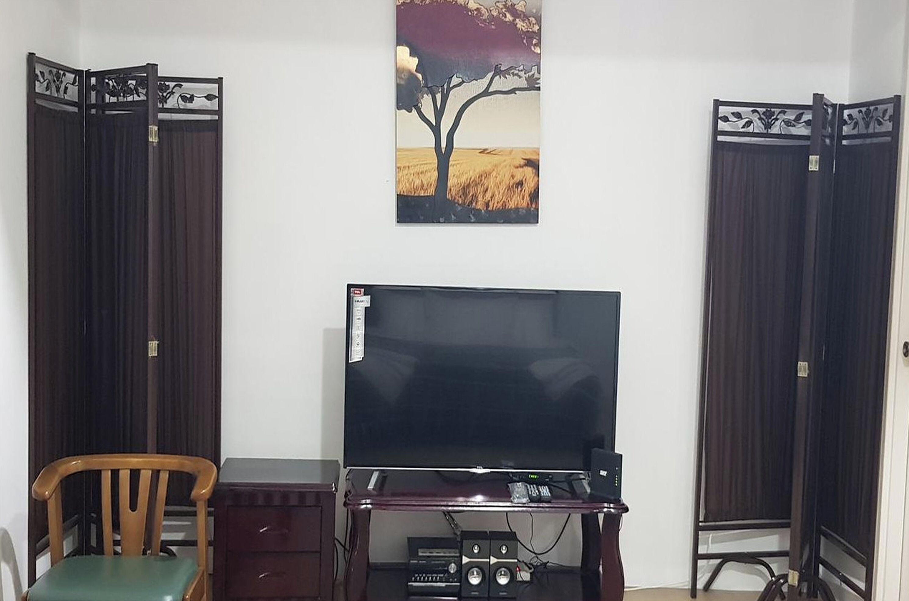 A room with a television on a wooden stand, a desk, a chair, and two dark-colored doors.