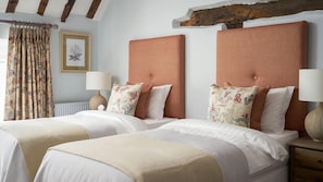 A double room with two beds, each with a headboard, bedside tables, lamps, and floral-patterned pillows.