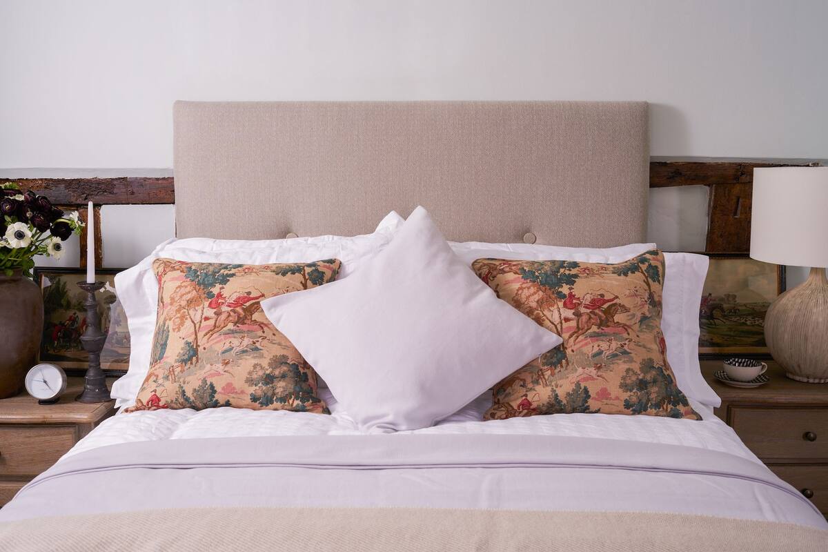 A neatly made bed with white linens, two decorative pillows with floral patterns, and a plain white pillow.