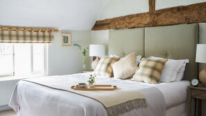 Un lit bien fait, avec un oreiller à carreaux, une table de chevet sur laquelle se trouve une lampe, et une fenêtre avec un rideau.