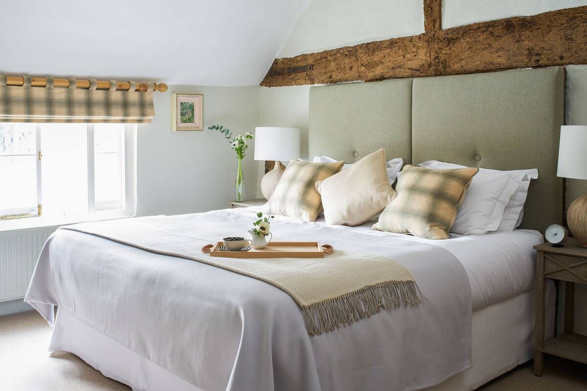 A neatly made bed with a checkered pillowcase, a bedside table with a lamp, and a window with a curtain.