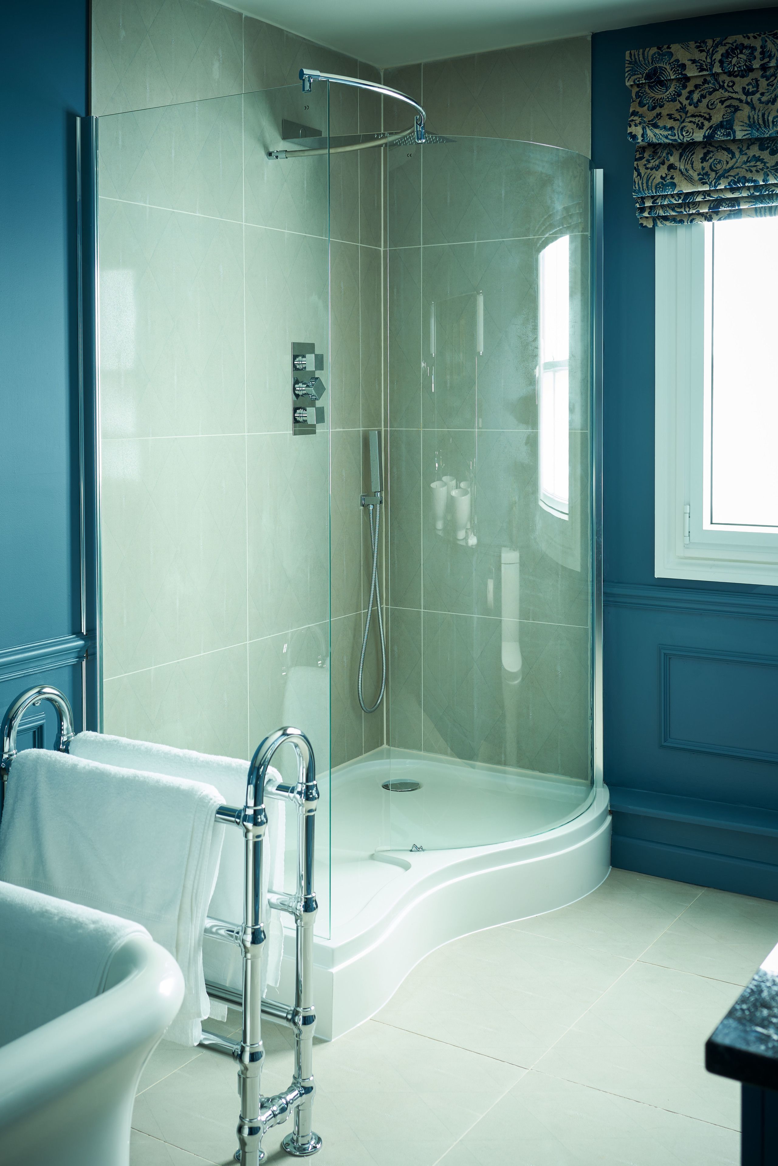 Un baño moderno con ducha de vidrio, bañera independiente y ventana con cortinas estampadas.