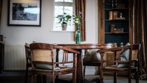 Une pièce chaleureuse avec une table et des chaises en bois, un tableau encadré au mur, une fenêtre avec des rideaux et une bibliothèque.