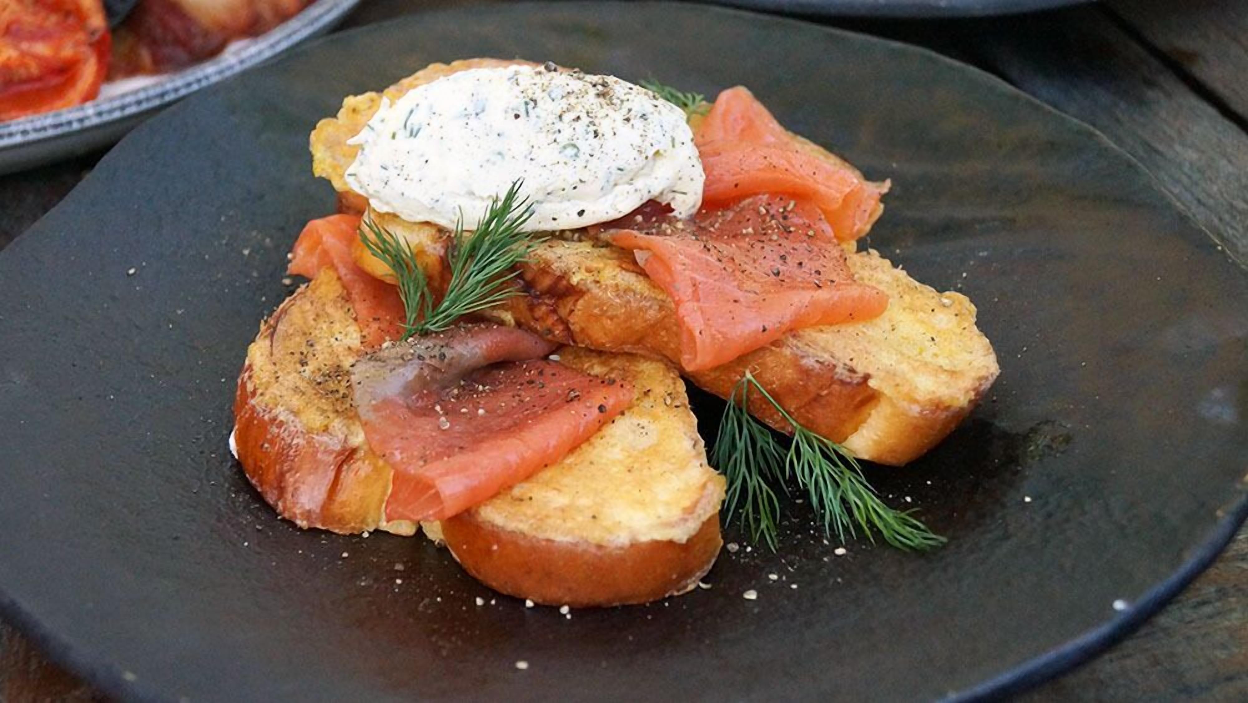 A plate with toast topped with smoked salmon, a poached egg, and a sprig of dill.