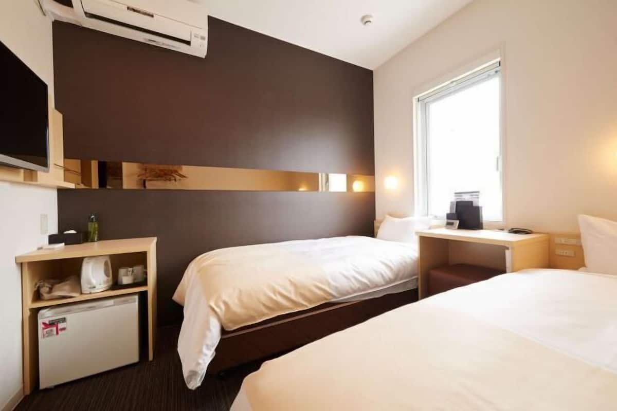 Habitación de hotel con dos camas, un escritorio, un refrigerador pequeño, un televisor y una ventana.