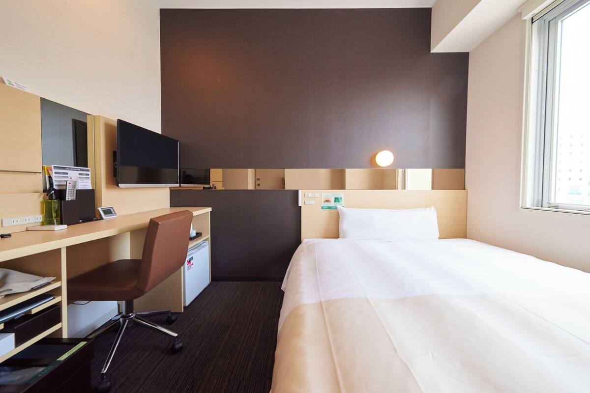 Una habitación de hotel con una cama, un escritorio con silla, televisión y un refrigerador pequeño.