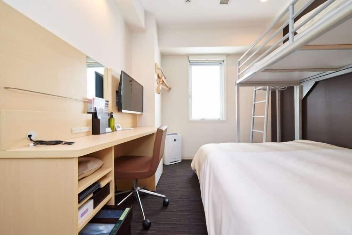 Una habitación de hotel con literas, un escritorio con silla, un televisor y una ventana.