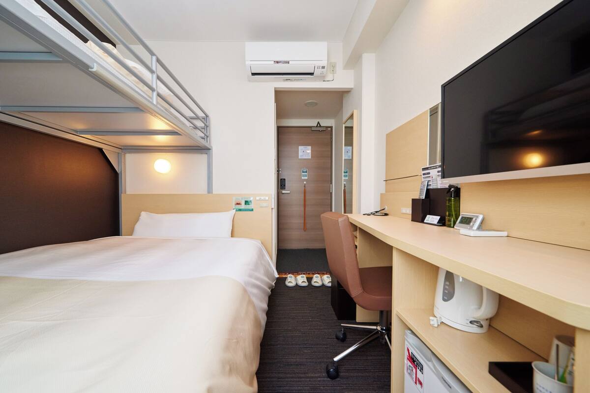 Habitación de hotel con cama, escritorio, silla, televisor y una pequeña kitchenette.