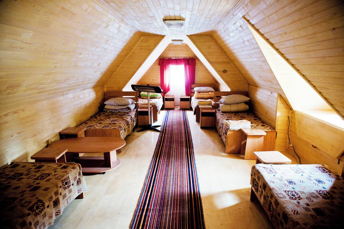 A cozy attic bedroom with wooden walls, a sloped ceiling, and a central bed with a striped runner.