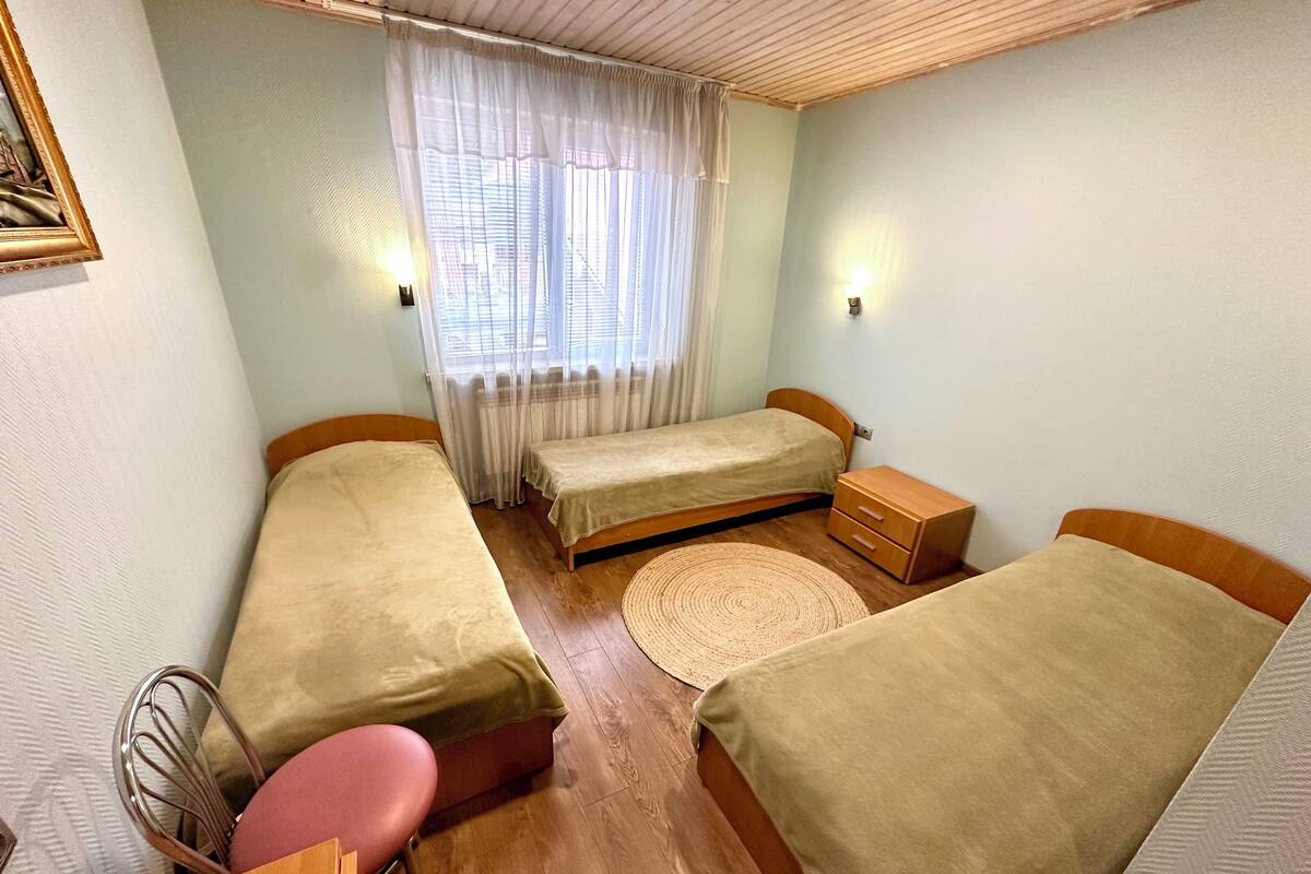 A small, cozy room with two single beds, a wooden dresser, a small table, and a chair.