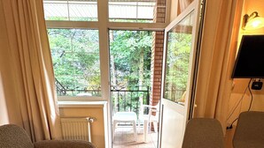 A room with a wooden floor, a sofa, two chairs, a sliding glass door leading to an outdoor area with a view of trees, and a radiator. - Agio Hotel (Kolochava)