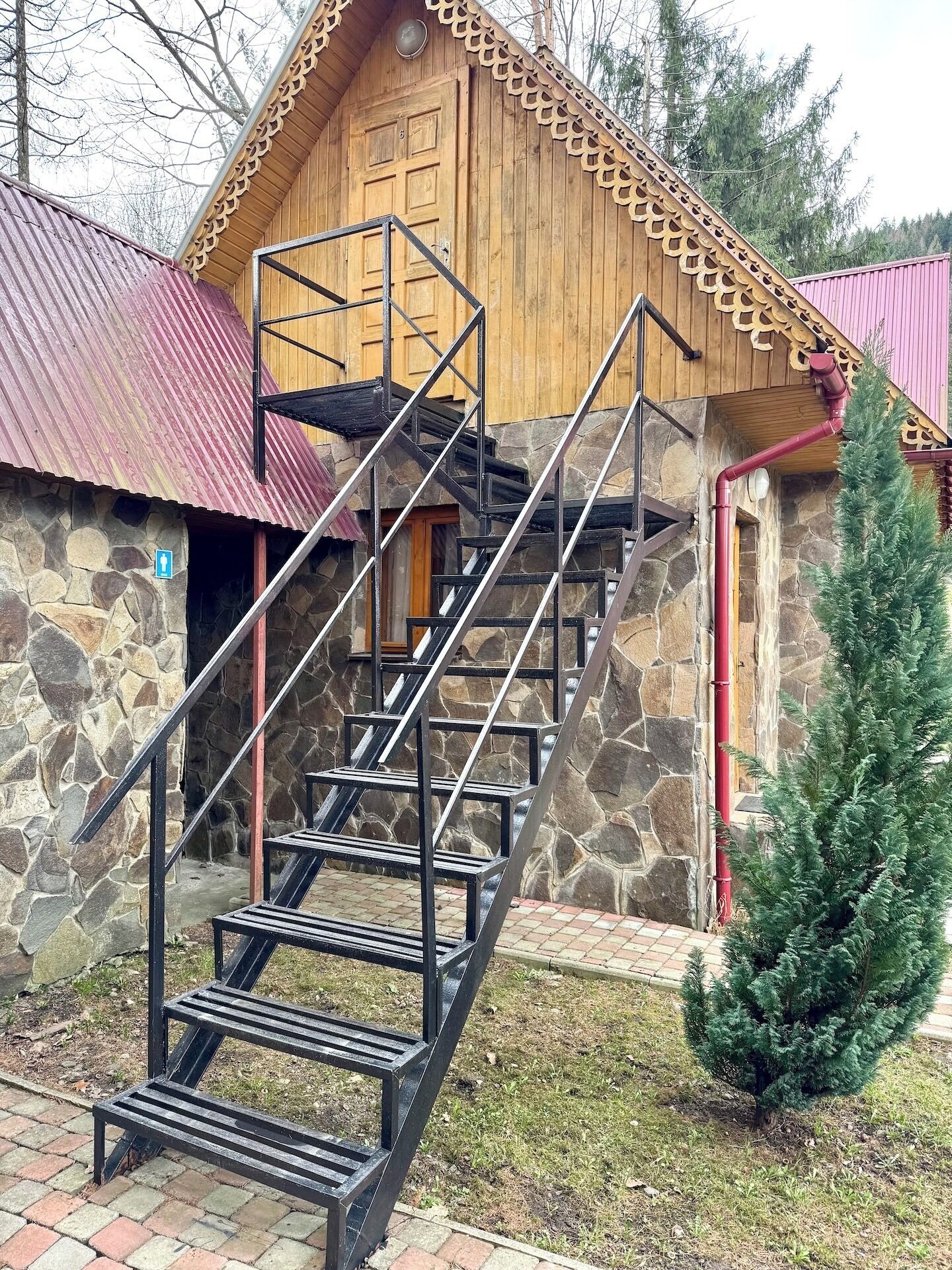 Una cabaña de madera con fachada de piedra y una escalera metálica que lleva a una puerta de madera.