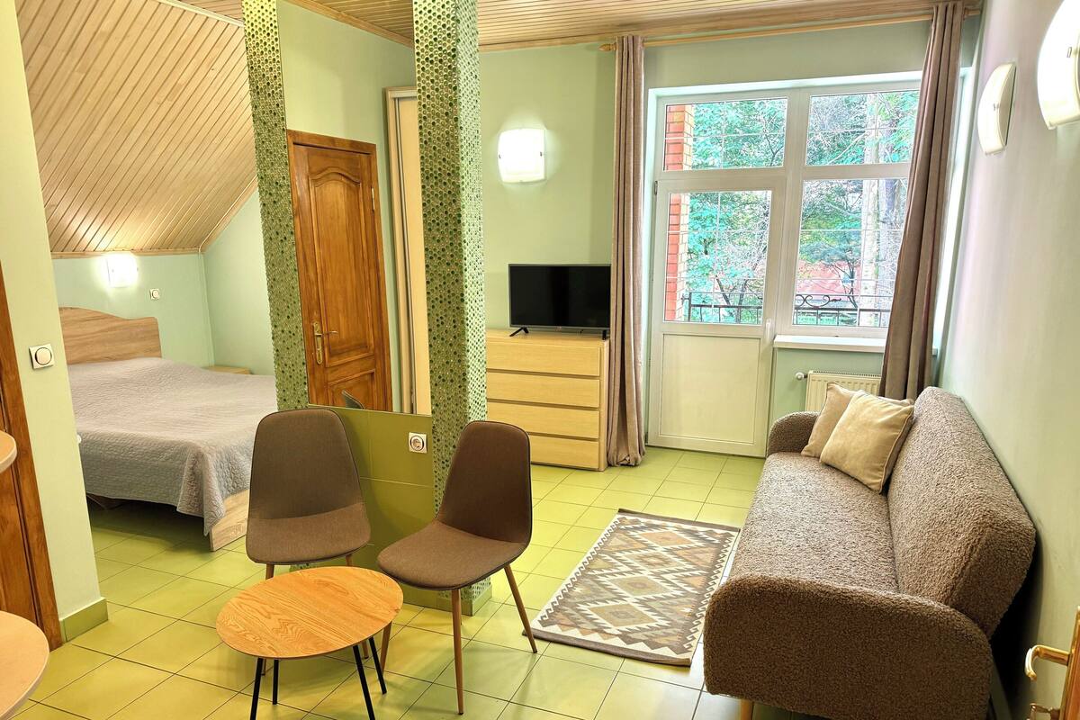 A room with a bed, two chairs, a sofa, a TV, and a window with curtains.