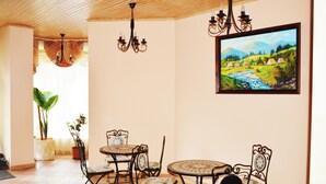 A dining area with a table and chairs, a chandelier, a painting, and potted plants. - Agio Hotel (Kolochava)