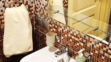 A bathroom with a white sink, a glass mirror, and a towel hanging on a rack.