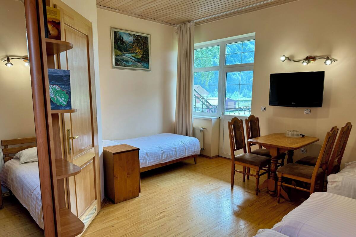 A room with a bed, a desk with chairs, a TV, and a painting on the wall.
