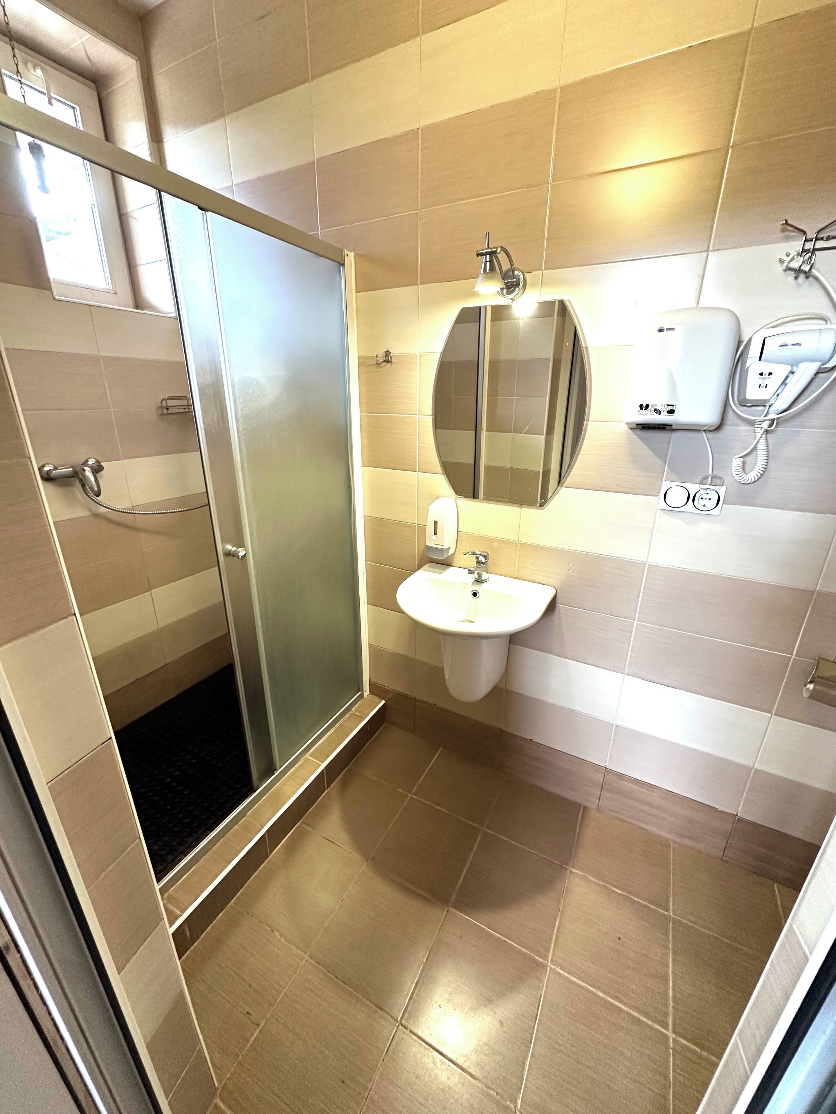 Un bagno moderno con cabina doccia in vetro, lavabo con specchio e asciugacapelli a parete.