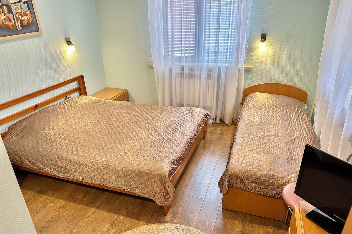 A bedroom with two beds, a wooden floor, and a television on a wooden stand.