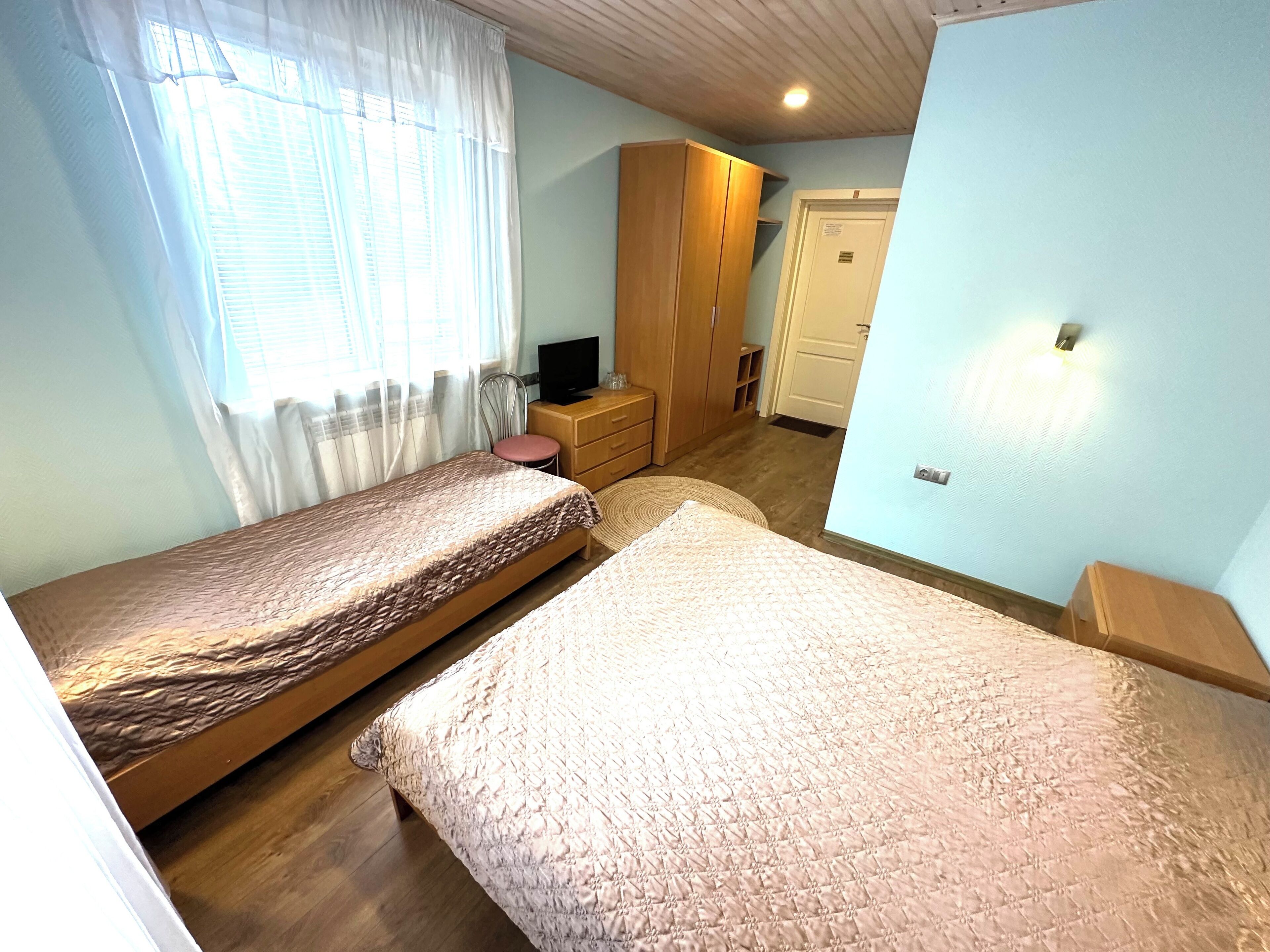 A bedroom with two single beds, a wooden wardrobe, a television, and a door leading to another room.