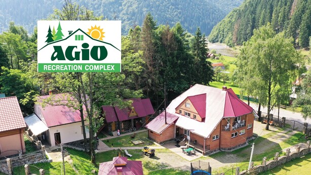 A rural area with a recreation complex named Agio, featuring multiple buildings with red roofs, a swimming pool, and a stone wall surrounding the property. - Agio Hotel (Kolochava)