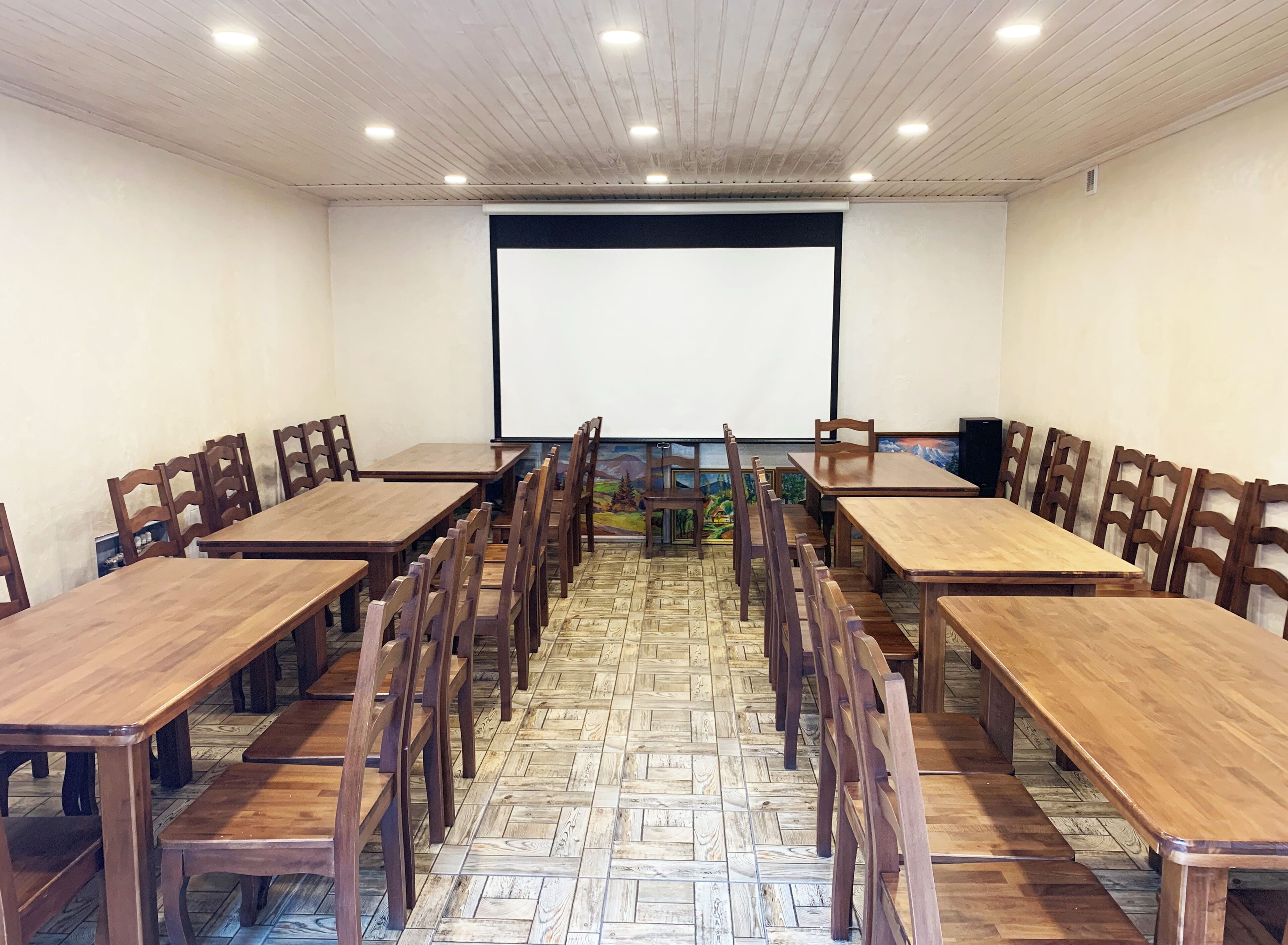 A conference room with wooden tables and chairs, a projector screen, and a tiled floor.