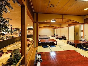 A traditional Japanese inn with tatami mat flooring, wooden furniture, and a view of a garden.