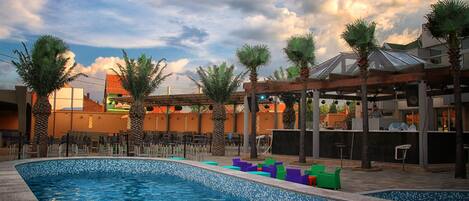 A swimming pool with a tiled edge, surrounded by palm trees and outdoor seating.