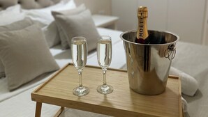 Una cama con ropa blanca, dos copas de champán y una botella de champán en un cubo sobre una bandeja.