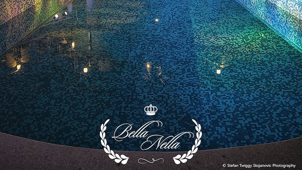 Un área de piscina nocturna con una estructura de tobogán circular, un espacio de relax con asientos y una piscina con mosaicos.