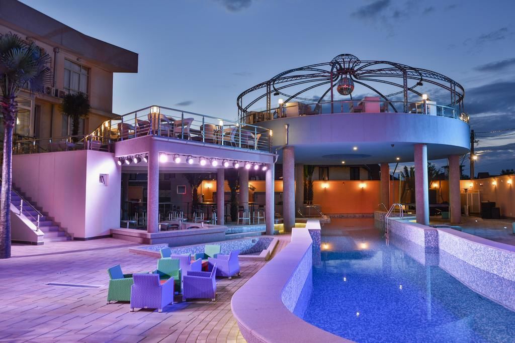 Un espace piscine agrémenté d’un élément décoratif aquatique circulaire, de chaises longues et d’un espace de détente couvert avec des tables.