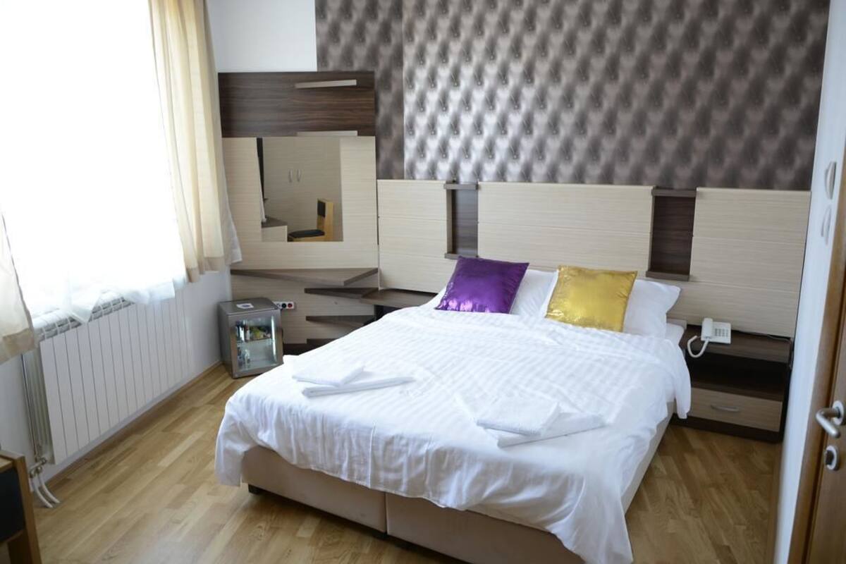 Habitación de hotel ordenada con una cama grande, una mesita de noche con teléfono y un espejo sobre la cama.