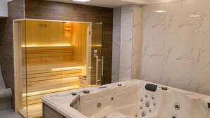 Un spa moderno con sauna de madera, un amplio jacuzzi y paredes de mármol.