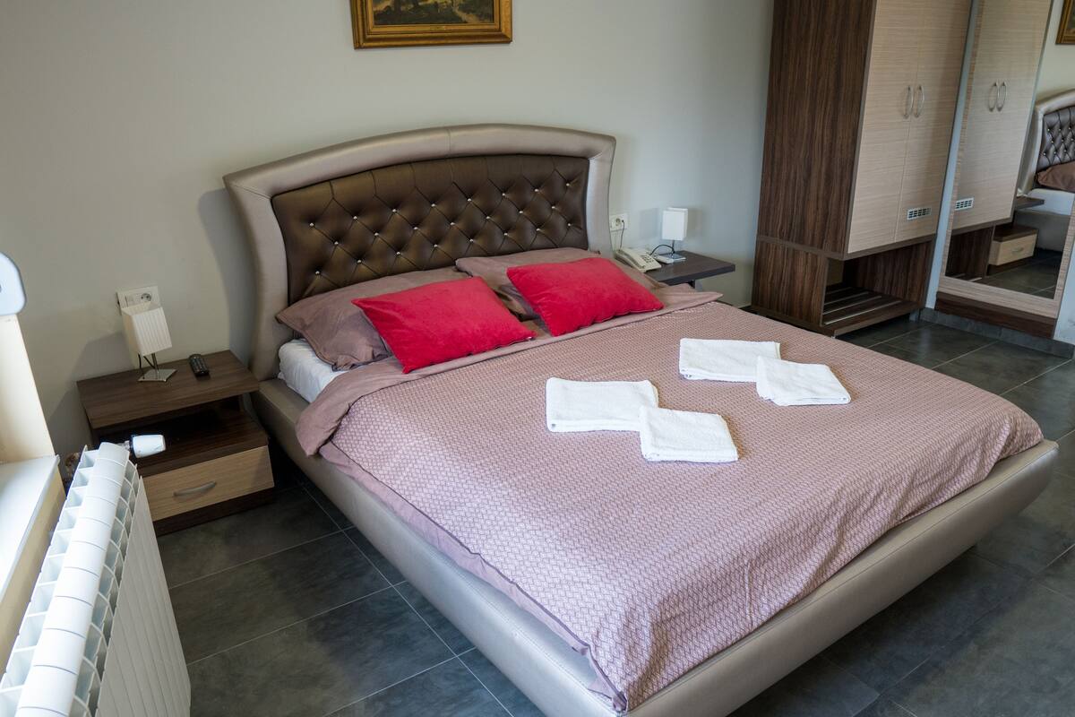 Una cama bien hecha con una colcha estampada, dos almohadas rojas y dos toallas blancas dobladas.